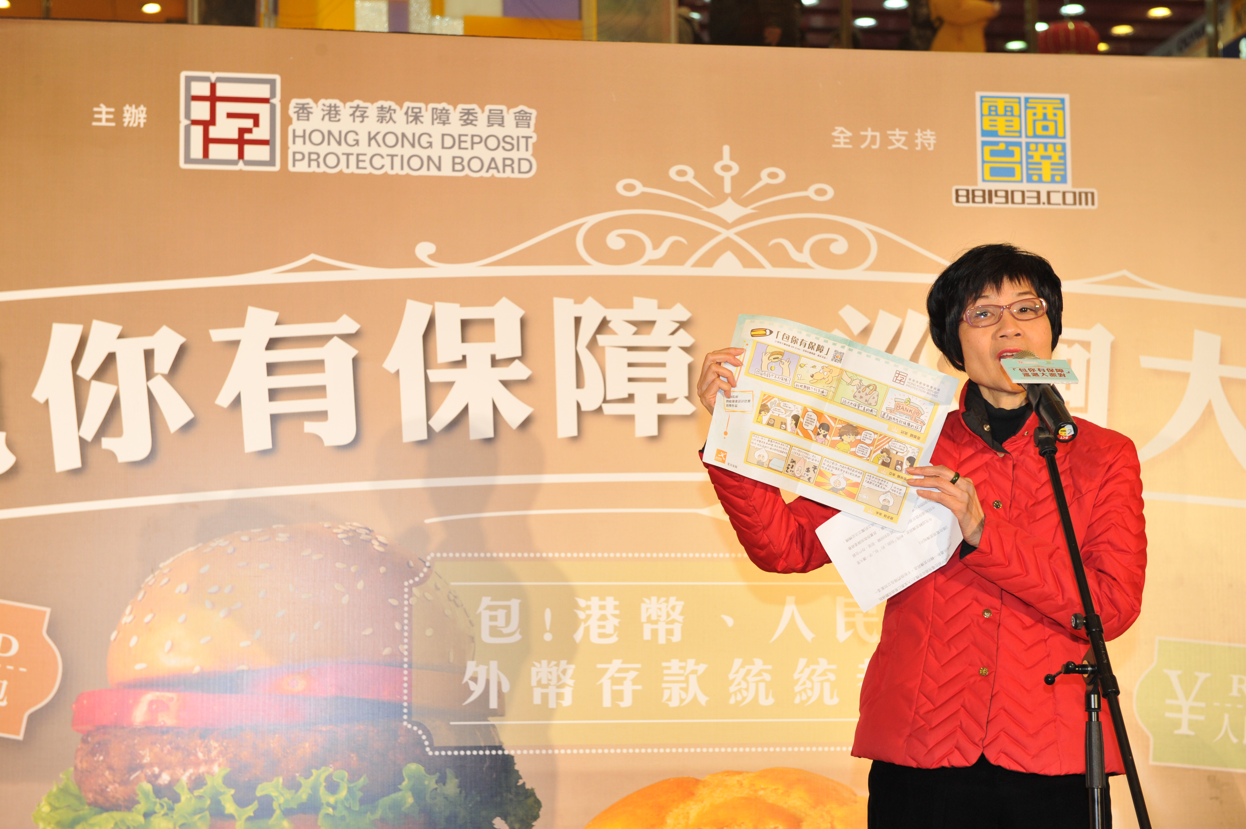 图二：存保会主席陈黄穗女士手持印上存保会彩色四格漫画设计比赛得奖作品的餐垫纸。